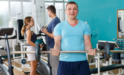Fototapeta na wymiar Sporty man doing strength exercises with barbell in gym