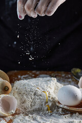 Female hands adding flour to dough, kneading dough for baking. Flour in the air