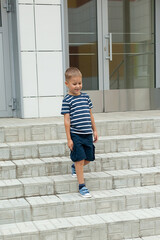 A small boy walks alone, leaves the building and goes down the steps. Kindergarten