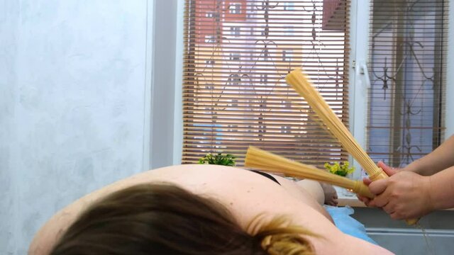 massage therapist makes an anti-cellulite massage to a fat woman on a massage table in a spa with a bamboo stick. Spa treatments. Health and beauty, diet