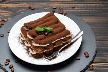 Classic tiramisu dessert on ceramic plate on wooden background
