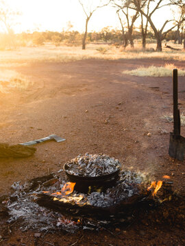 Cooking a roast dinner in a camp oven, over hot coals, as a golden, warm, sun sets. Shot in Outback Australia