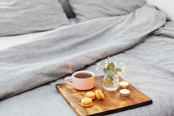 Obraz na płótnie Canvas cup of tea with macaroons and candles on wooden tray on bed