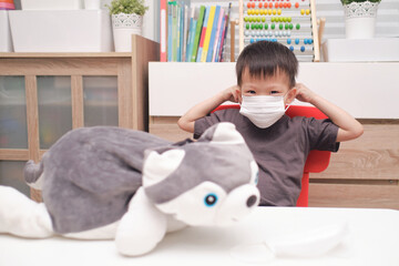 Happy smiling little Asian boy child putting protective medical mask by himself by himself at home during the Covid-19 health crisis, New normal lifestyle concept