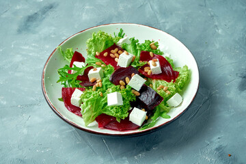 Healthy salad with boiled beets, feta cheese and pine nuts in a white bowl on a gray background