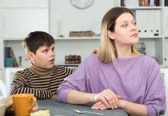 Small boy wants to make peace with his mother after arguing at table in kitchen