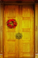 Wooden patterned doors of golden color with carved platbands and with a New Year's wreath hanging on one of the doors