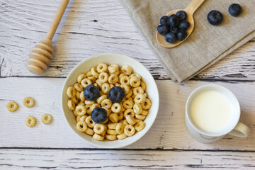 Honey rings with blueberries and milk in a bowl on the wooden background. Copy space. Top view. Flat lay. Horizontal orientation.