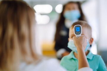 Temperature screening and medical check at school. Child in face mask in class in covid-19 outbreak. Teacher with thermometer at preschool entrance. 