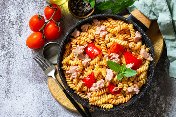 Healthy lunch. Fusilli pasta with canned tuna, grilled red peppers and tomatoes in frying pan on a stone countertop. Top view flat lay background. Copy space.
