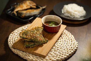 Thai foods, Acacia Pennata Omelette with Shrimp-paste place on a wooden board on Hand Weaving placemat and on a dark wooden table surrounded with Fries Short Mackerels sauce and Jasmine rice