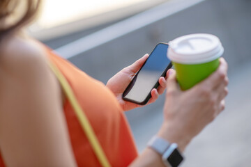 Close up picture of a woman holding a smartphone and cup of coffee