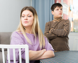 Upset mother sitting at table after arguing with son in domestic interior