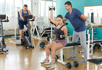Personal trainer helping young woman with exercise technique at sport club