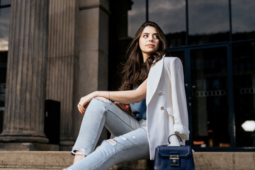 Obraz na płótnie Canvas Attractive woman wearing white fashion jacket and jeans look away. Young woman on building background