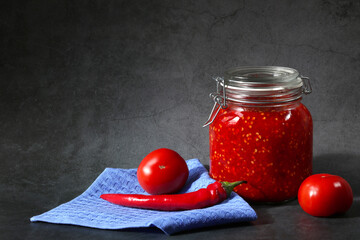 Ground hot red pepper with tomatoes in a glass jar on a dark background. A spicy seasoning made from pepper and tomatoes at home. Home cooking.