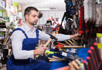 young positive male is standing with new hammer in tools store.