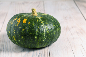 small green pumpkin lies on light wooden background