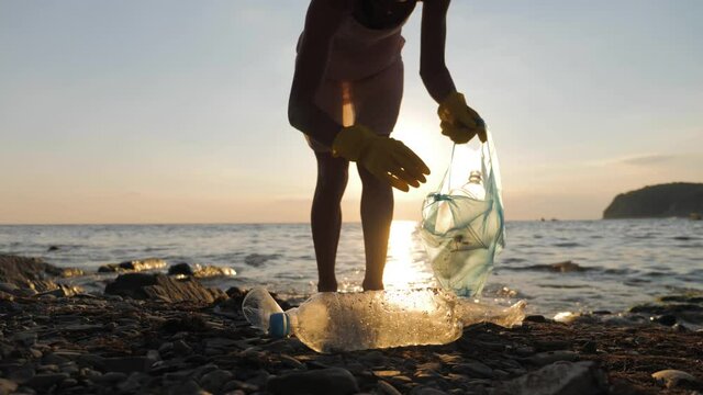 Volunteer girl collects trash in the trash bag. Plastic bottles and other trash on sea beach. Environmental pollution and ecological problem concept.