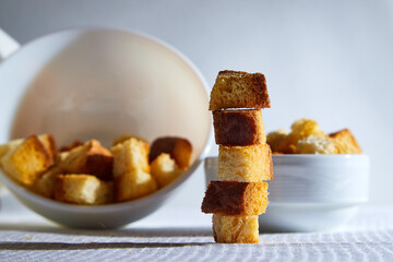 Square toasted pieces of homemade delicious rusk, hardtack, Dryasdust, zwieback stand in columns near white plate on a white tablecloth.