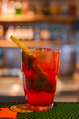 Red fruit cocktail drink with raspberry, mint and ice on dark rustic wooden table in a bar or restaurant.