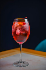 A glass with the red citrus cocktail. Alcohol summer beverage in a wine glass. Refreshing drink with ice.