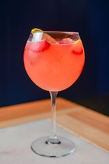 Citrus fruit cocktail in nice red color in front of a black background. Served in a wine glass on a wooden table.