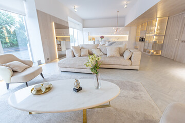 trendy modern interior design of a large studio in white and beige colors with large floor-to-ceiling windows. area of ​​white kitchen with an island and a recreation area