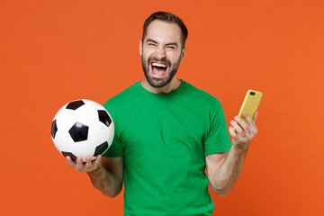 Laughing young man football fan in green t-shirt cheer up support favorite team with soccer ball...