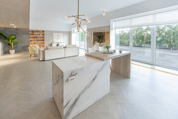 trendy modern interior design of a large studio in white and beige colors with large floor-to-ceiling windows. area of ​​white kitchen with an island and a recreation area