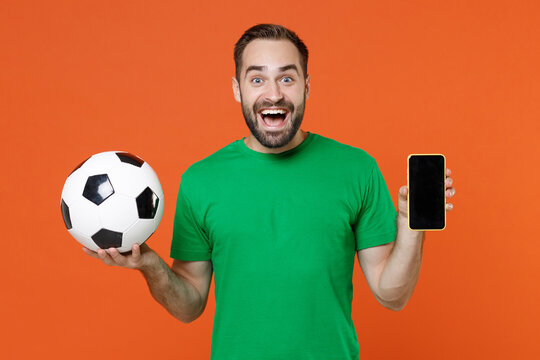 Excited Young Man Football Fan In Green T-shirt Cheer Up Support Favorite Team With Soccer Ball Hold Mobile Phone With Blank Empty Screen Isolated On Orange Background. People Sport Leisure Concept.