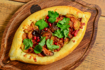 Traditional boat-shaped Adjarian khachapuri with meat and fresh greenery filling in the middle.