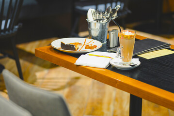 Still life details, cup of coffee, piece of cake and opened journal on a table in restaurant or cafe.