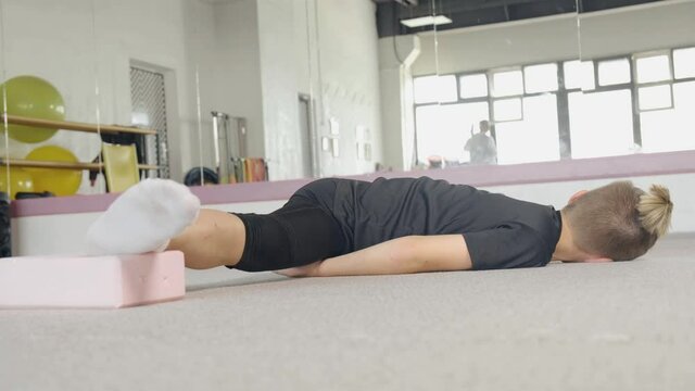 A young guy performs flexibility exercise lying on the floor and help himself with his hands. Flexible, beautiful body. The concept of sports and meditation. Stretching and yoga workout.