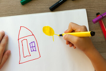 A small child draws a house with markers in the album. Step-by-step instructions