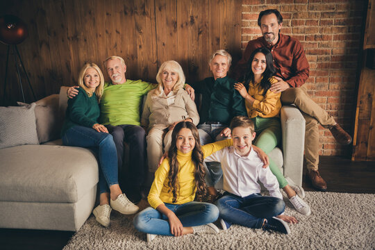 Photo of full family eight people gathering cuddle embrace satisfied good season time friendship company two little kids floor carpet sitting sofa generation in evening living room indoors