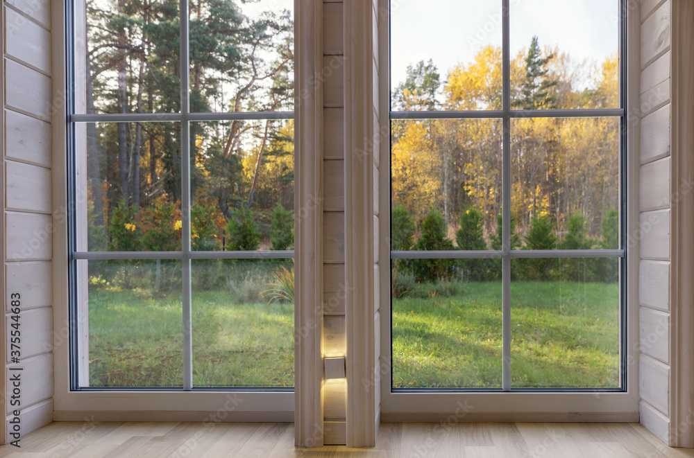 Wall mural bright interior of the room in wooden house with a large window overlooking the autumn courtyard.