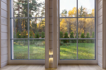 Bright interior of the room in wooden house with a large window overlooking the autumn courtyard.