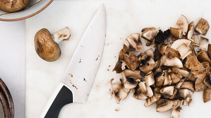 Chopped fresh raw organic baby bella mushrooms close up on marble cutting board, flat lay