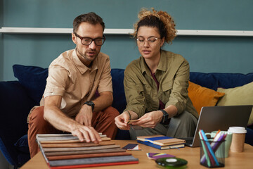 Two designers sitting on sofa and working with fabric samples they discussing new fashion project