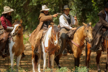 
Three cowboys on horseback stand in the forest and carry guns.