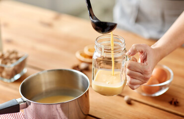 christmas and seasonal drinks concept - close up of hands with ladle pouring eggnog from pot to glass mug at home