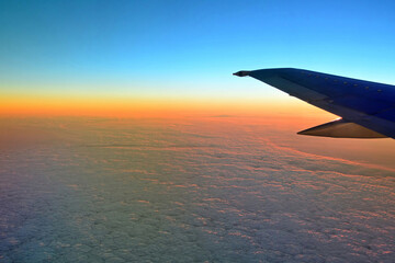 Fototapeta premium Blurred view of aircraft wing silhouette with blue sky horizon and clouds background in sun set time, viewed from airplane window