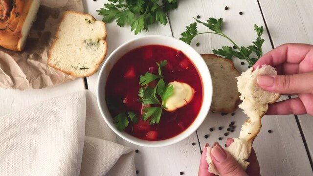 A girl breaks soft fresh bread near a plate of vegetable beet soup