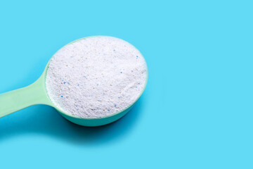 Detergent powder in measuring spoon on blue background. Laundry concept.