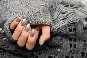 Female hand with silver nail design. Silver nail polish manicured hand. Woman hands hold grey wool...