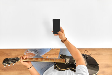 leisure, music and people concept - young man or musician with guitar and smartphone sitting at...