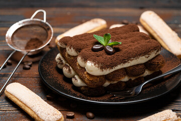 Classic tiramisu dessert on ceramic plate and savoiardi cookies on wooden background