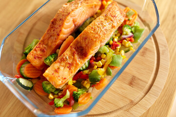 food, eating and culinary concept - close up of salmon fish with vegetables in baking dish on kitchen table at home