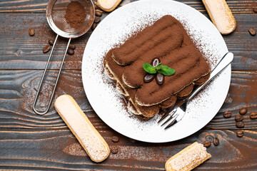 Classic tiramisu dessert on ceramic plate and savoiardi cookies on wooden background